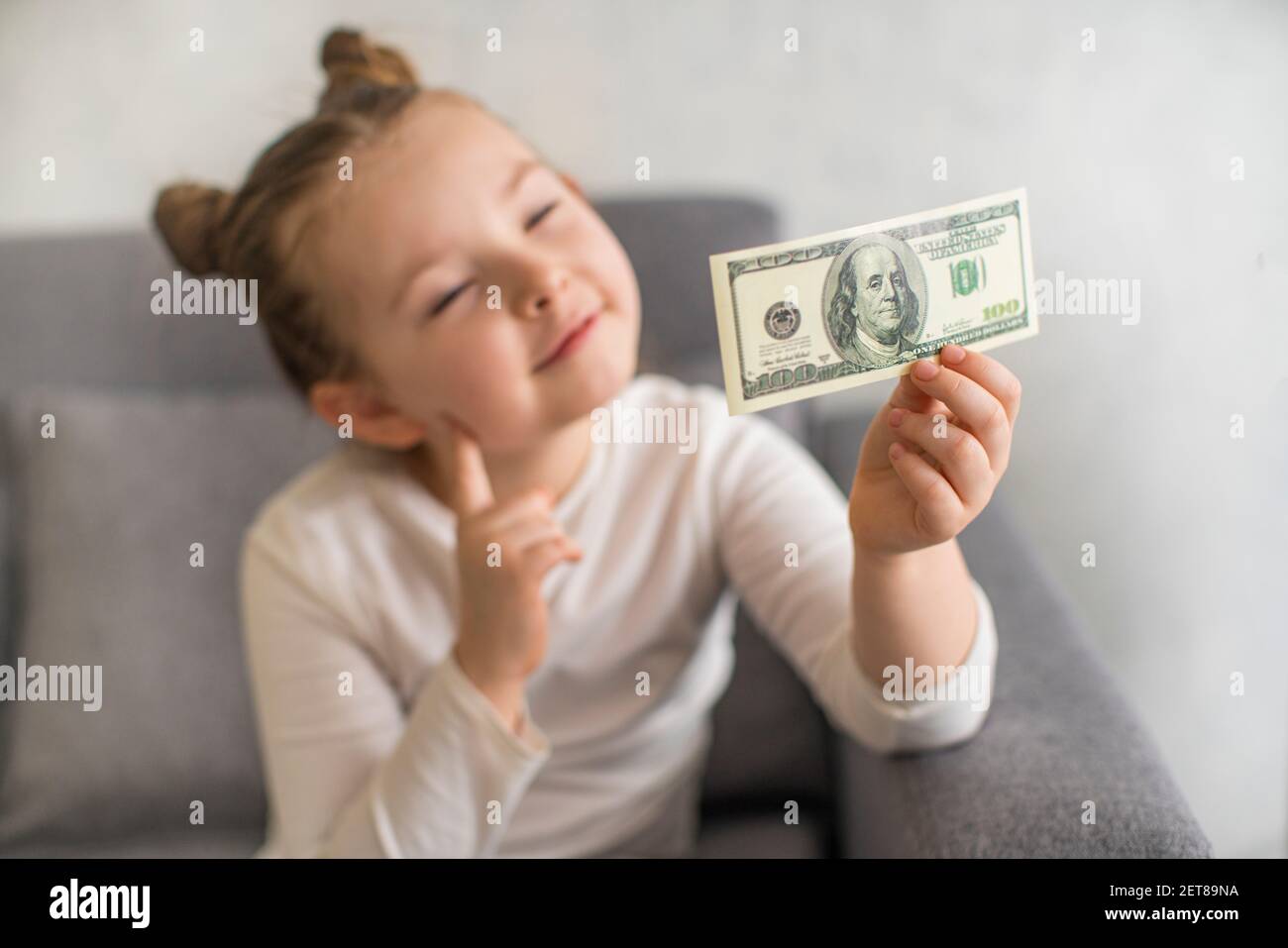 Niña pequeña y linda con el billete del dólar estadounidense como símbolo de la educación financiera. Enfoque selectivo. Foto de alta calidad Foto de stock