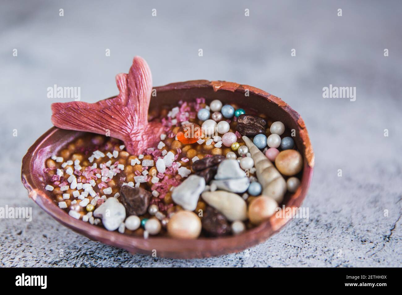 Medio huevo de chocolate relleno de arroz con relleno. El huevo está decorado con piedras preciosas multicolores y una cola de sirenas Foto de stock