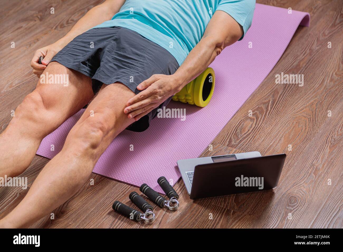 un hombre de 50 años realiza ejercicios mientras está acostado en la alfombra en casa, mirando la computadora. Durante una pandemia, una persona entrena en un apartamento a través del Foto de stock