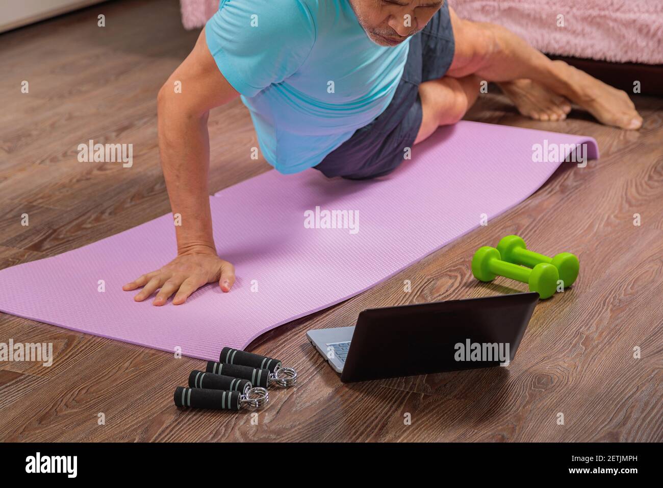 un hombre de 50 años realiza ejercicios mientras está acostado en la alfombra en casa, mirando la computadora. Durante una pandemia, una persona entrena en un apartamento a través del Foto de stock