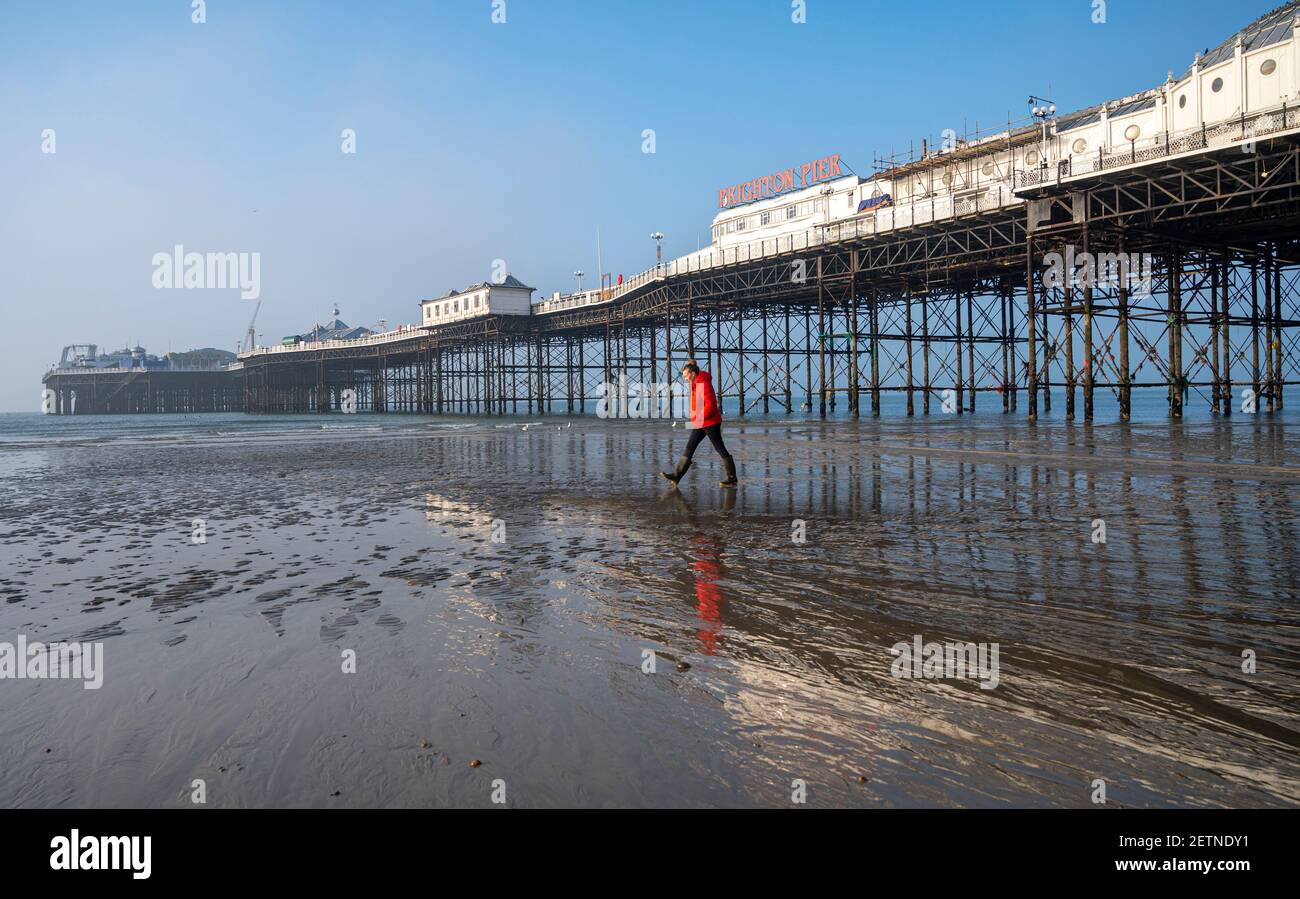 Brighton Reino Unido 2 de marzo de 2021 - un caminante hace la mayor parte de la marea baja en la playa de Brighton en el muelle como el sol comienza a romper a través de la niebla temprano esta mañana: Crédito Simon Dack / Alamy Live News Foto de stock