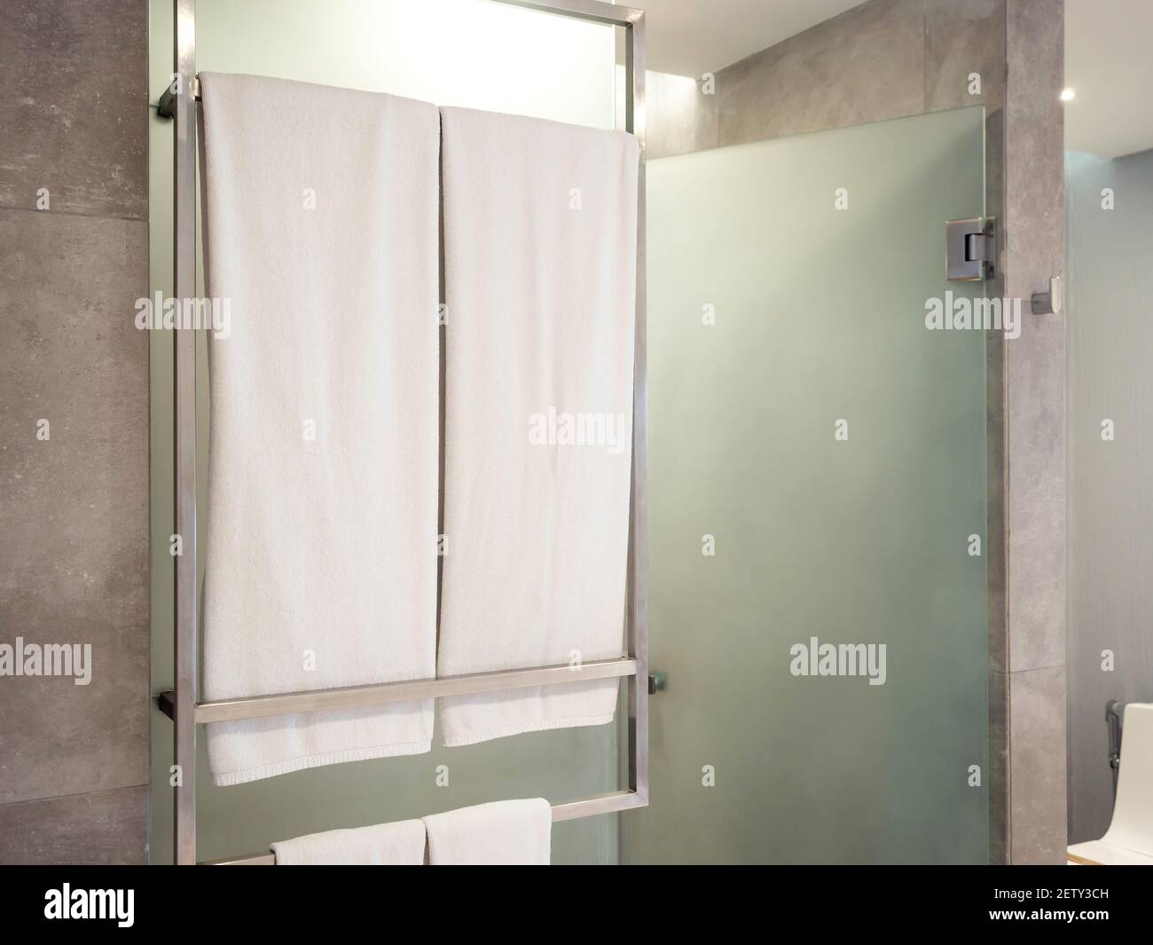Dos juegos de toallas blancas limpias en el perchero frente a la ducha de  cristal esmerilado en el baño moderno preparando para los huéspedes en el  hotel Fotografía de stock - Alamy