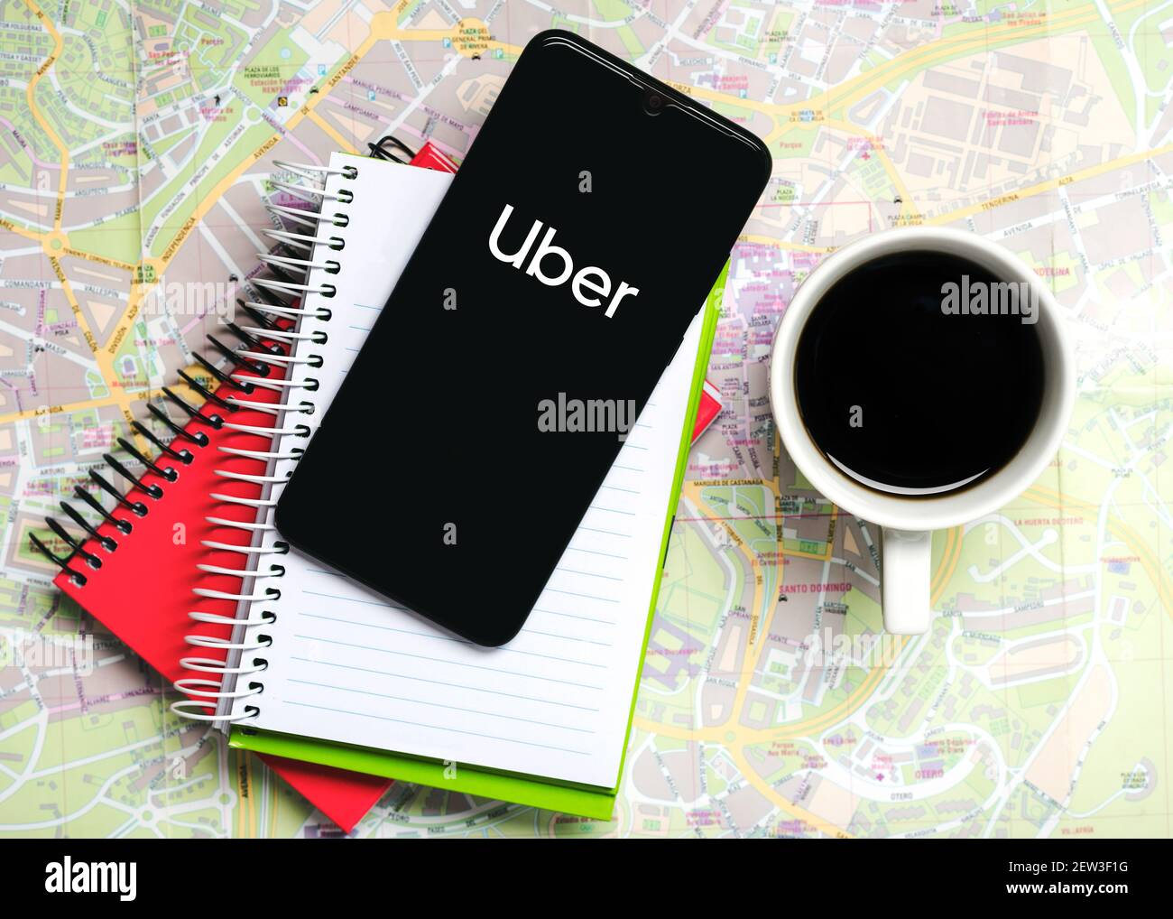 Icono de la aplicación Uber en la pantalla negra del smartphone con portátiles y una taza de café en un mapa de carreteras Foto de stock