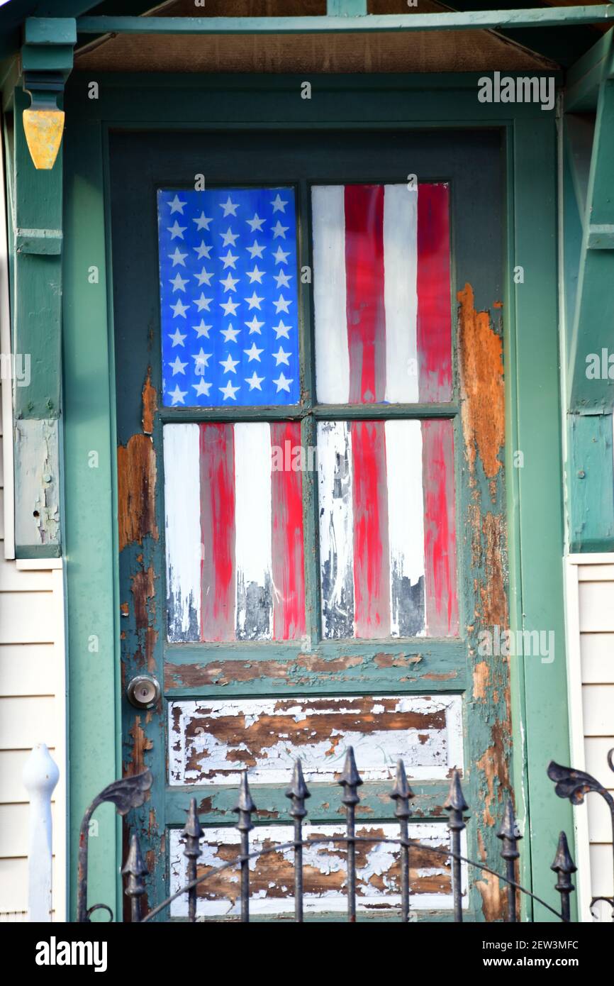 Una bandera americana hecha jirones cuelga dentro de una ventana de puerta Foto de stock