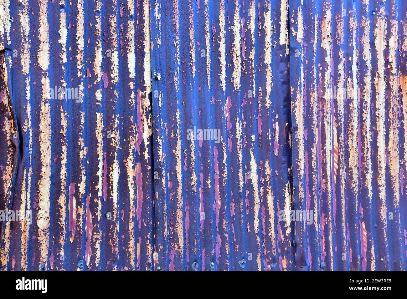 Una pared de estaño está pintada con tonos de púple y atada a un fondo perfectamente abstracto, muy texturizado. Foto de stock