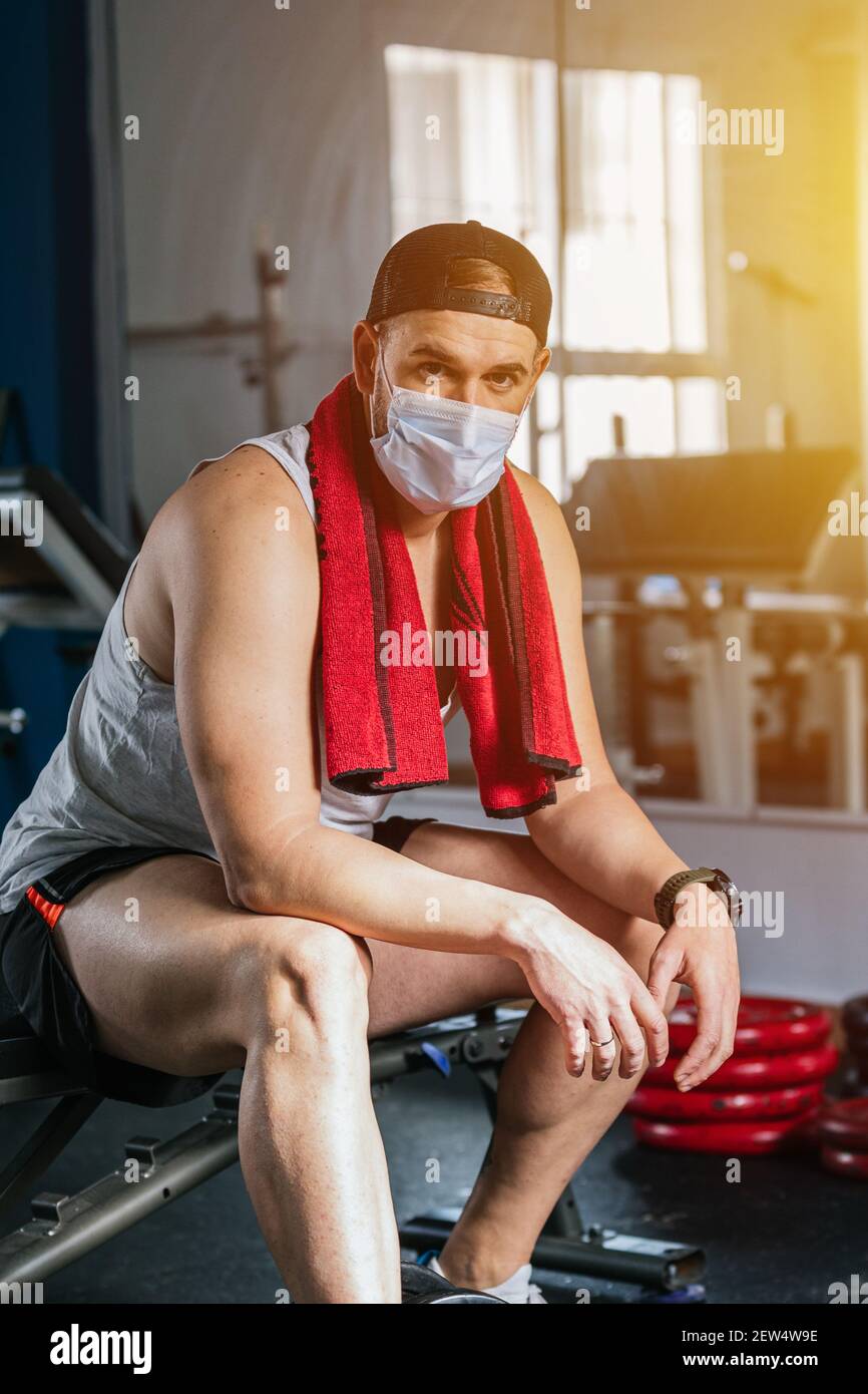 Hombre sentado en el gimnasio con una toalla alrededor del cuello. Rodeado  de máquinas y pesas. Concepto de salud y bienestar Fotografía de stock -  Alamy