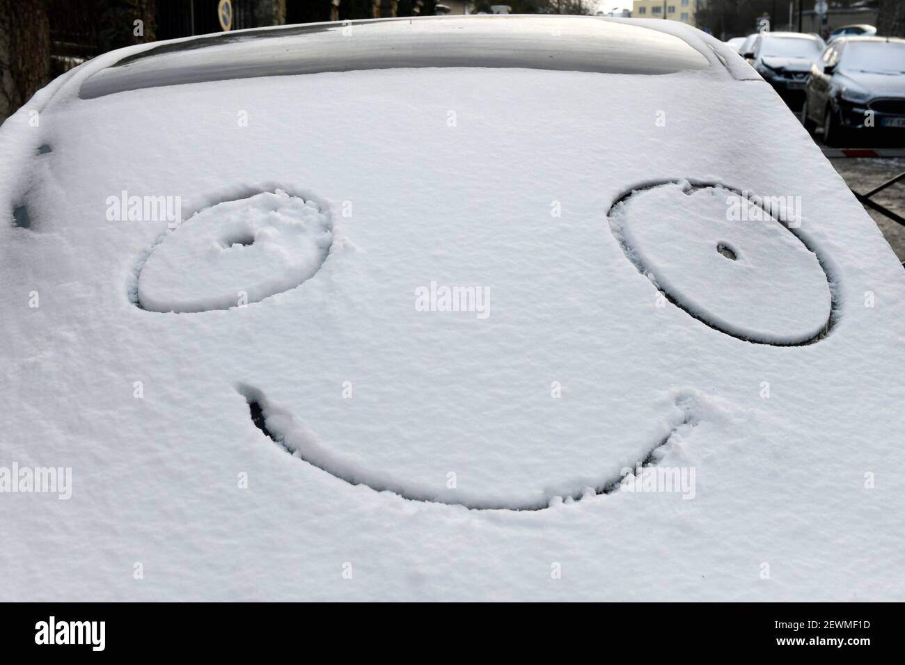 Emoticono dibujado en la nieve en la parte delantera de un coche en Sartrouville, Yvelines, Francia. Foto de stock