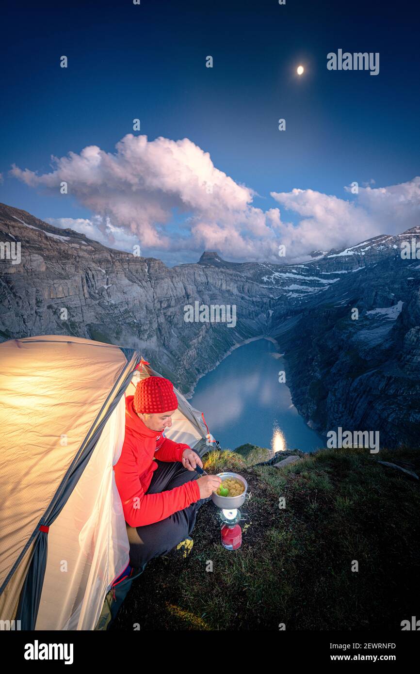 El hombre hiker cocinando mientras acampaba en una tienda sobre el lago Limmernsee, Cantón de Glarus, Suiza, Europa Foto de stock