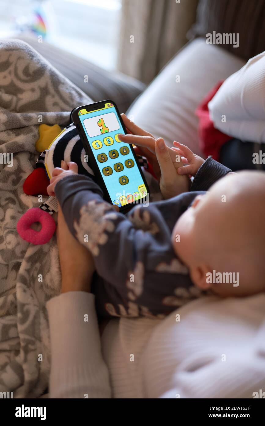 La primera introducción de Baby a la pantalla de tiempo mientras juega y toca en un teléfono móvil la aplicación de los niños aprender números con su mamá. Foto de stock