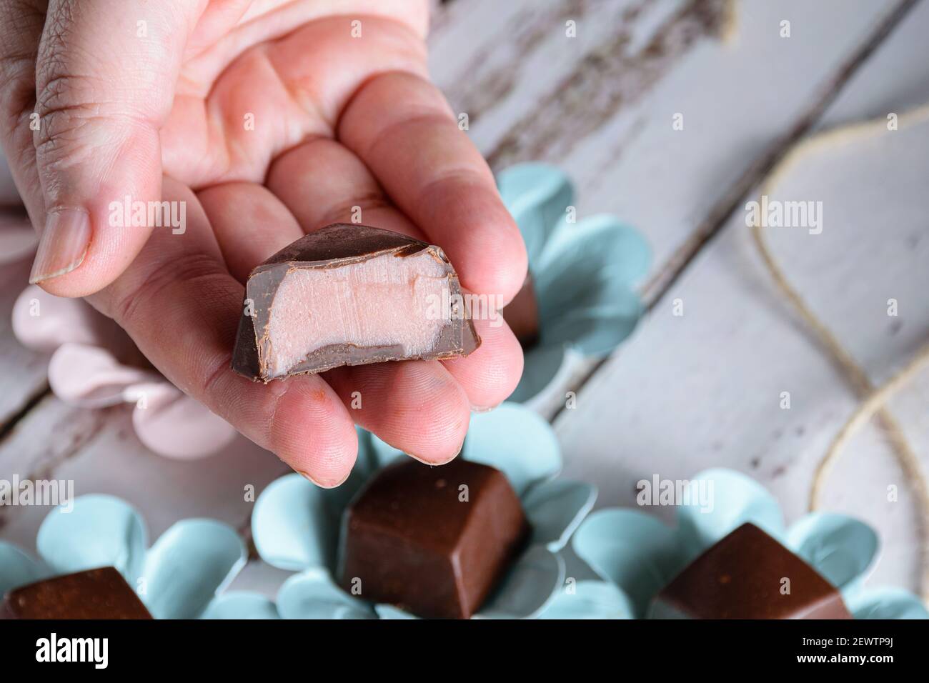 Mano sosteniendo un bonbón de chocolate cortado a la mitad, mostrando relleno de ganache rosa. Foto de stock