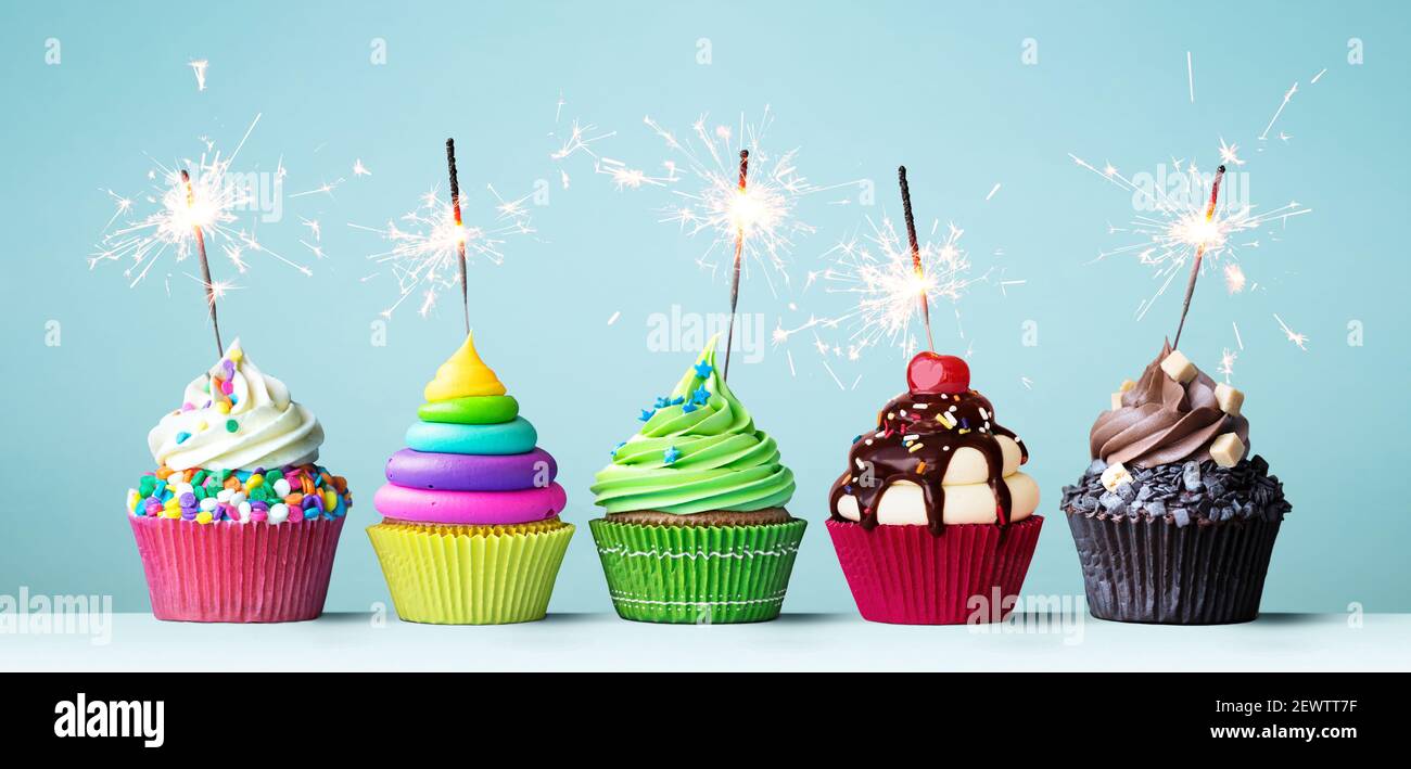 Surtido de pasteles de celebración de colores brillantes decorados con sparklers para una fiesta de cumpleaños Foto de stock