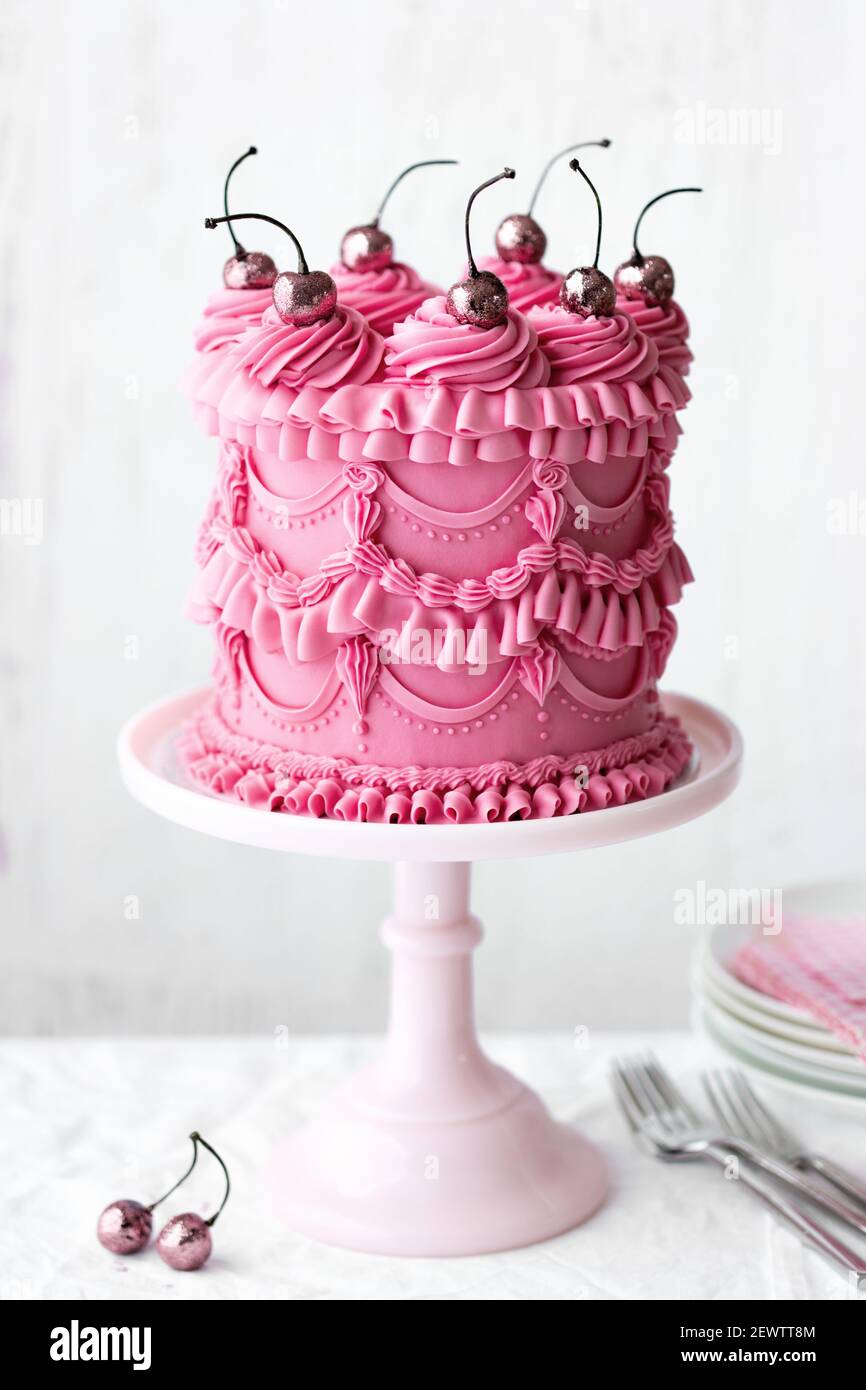Pastel de celebración rosa con crema de mantequilla vintage con florituras y cerezas Foto de stock