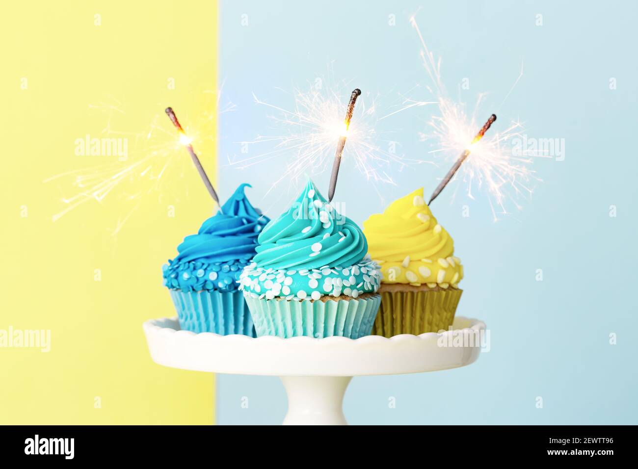 Cupcakes de celebración decorados con espumantes azules y amarillos y sparklers para una fiesta de cumpleaños Foto de stock