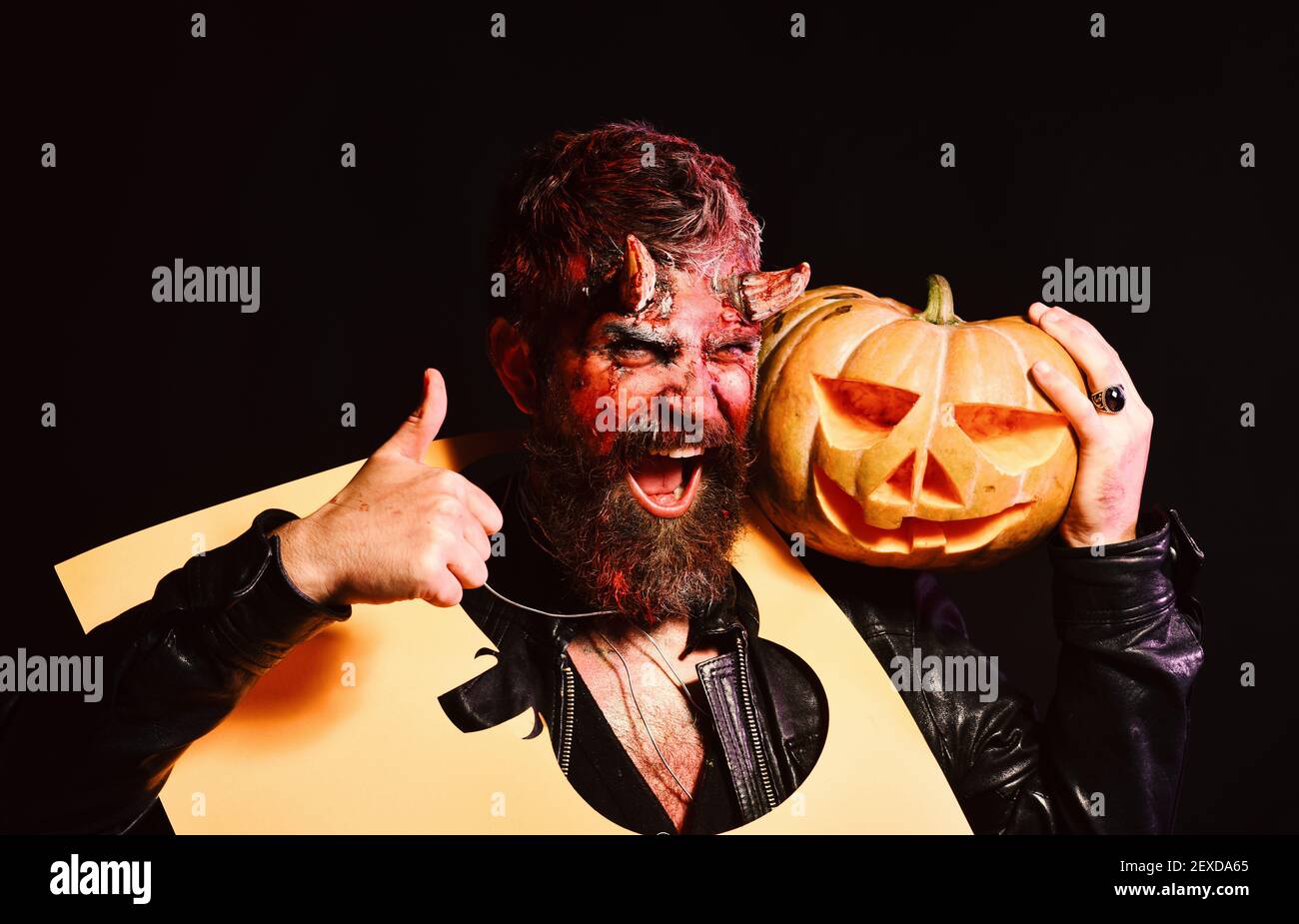 Monster celebra el festival. Concepto de fiesta de Halloween. Hombre que lleva maquillaje mantiene la silueta de calabaza en el cuello sobre fondo negro. Demonio con cuernos y cara feliz sostiene Jack Monster celebra el festival. Concepto de fiesta de Halloween. Hombre que lleva maquillaje mantiene la silueta de calabaza en el cuello sobre fondo negro. Demonio con cuernos y cara feliz sostiene Jack