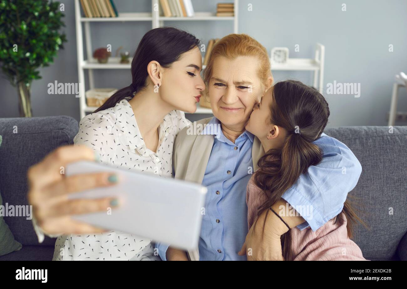 Feliz hija y nieta besando a la abuela y tomando selfie encendido smartphone Foto de stock