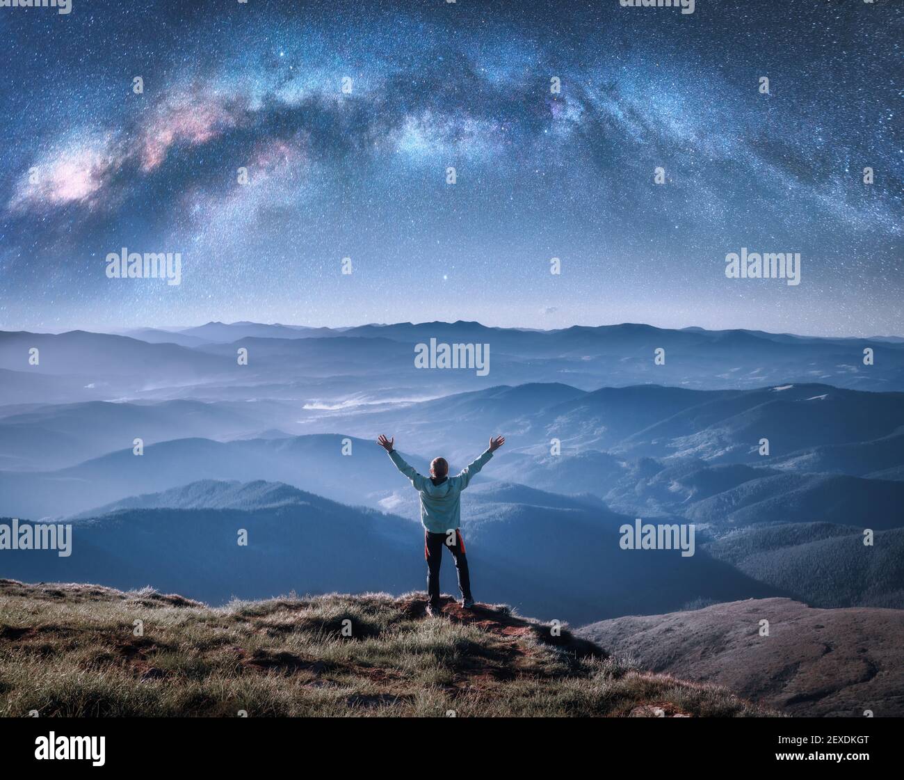 Hombre feliz en el pico de montaña y arco vía Láctea Foto de stock