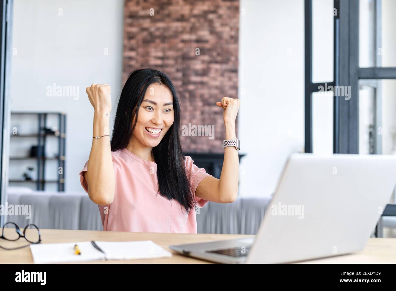 Una mujer asiática demasiado alegre con un ordenador portátil en casa, viendo en la pantalla y gritando alegremente, emocionada mujer consiguió contratar trabajo, obtener buenas noticias o ganó en la lotería. Concepto de victoria Foto de stock