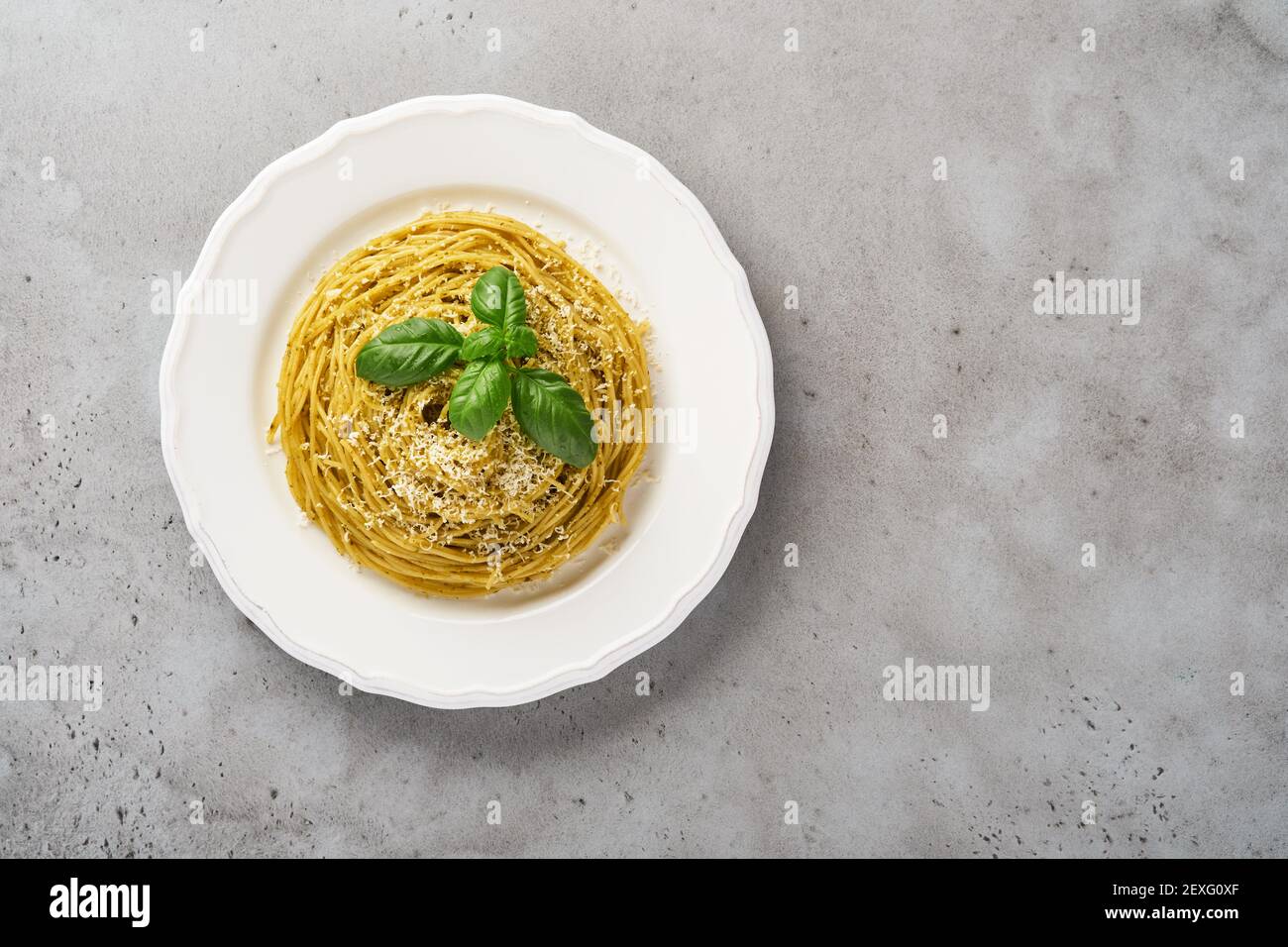 Espaguetis de pasta con salsa de pesto y hojas frescas de albahaca en un tazón blanco. Fondo gris. Se burlan. Vista superior. Foto de stock