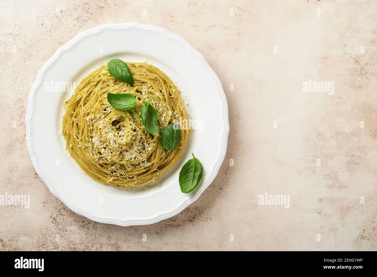 Espaguetis de pasta con salsa de pesto y hojas frescas de albahaca en un tazón blanco. Fondo gris. Se burlan. Vista superior. Foto de stock