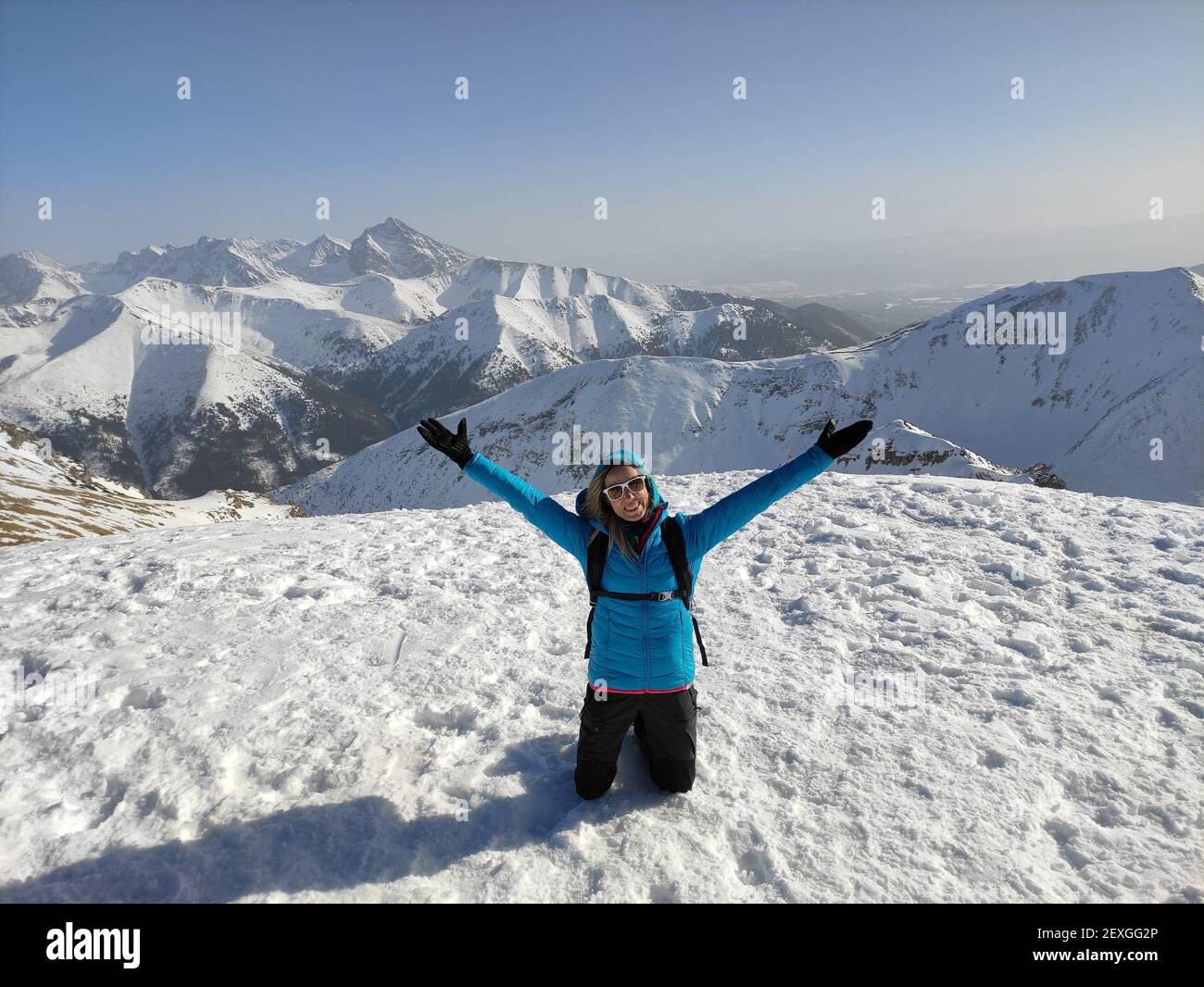 Feliz mujer turística en una chaqueta azul y los brazos levantados en la cima de una montaña. Foto de stock
