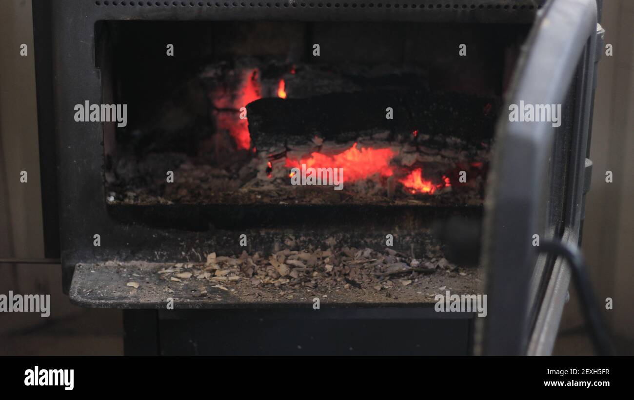 Agregar madera a una estufa de madera durante los fríos meses de invierno. Foto de stock