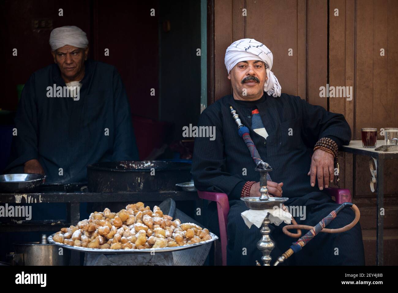 Retrato de un egipcio local fumando una pipa de shisha junto a un plato de dulces fritos en un café (ahwa) en el barrio islámico de el Cairo, Egipto Foto de stock