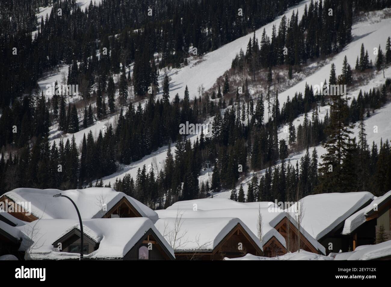 Nieve en los tejados de los chalets de esquí con pistas de esquí en la estación de esquí de Columbia Británica en el fondo de la habitación de formato horizontal para el tipo de techo triangular casa Foto de stock