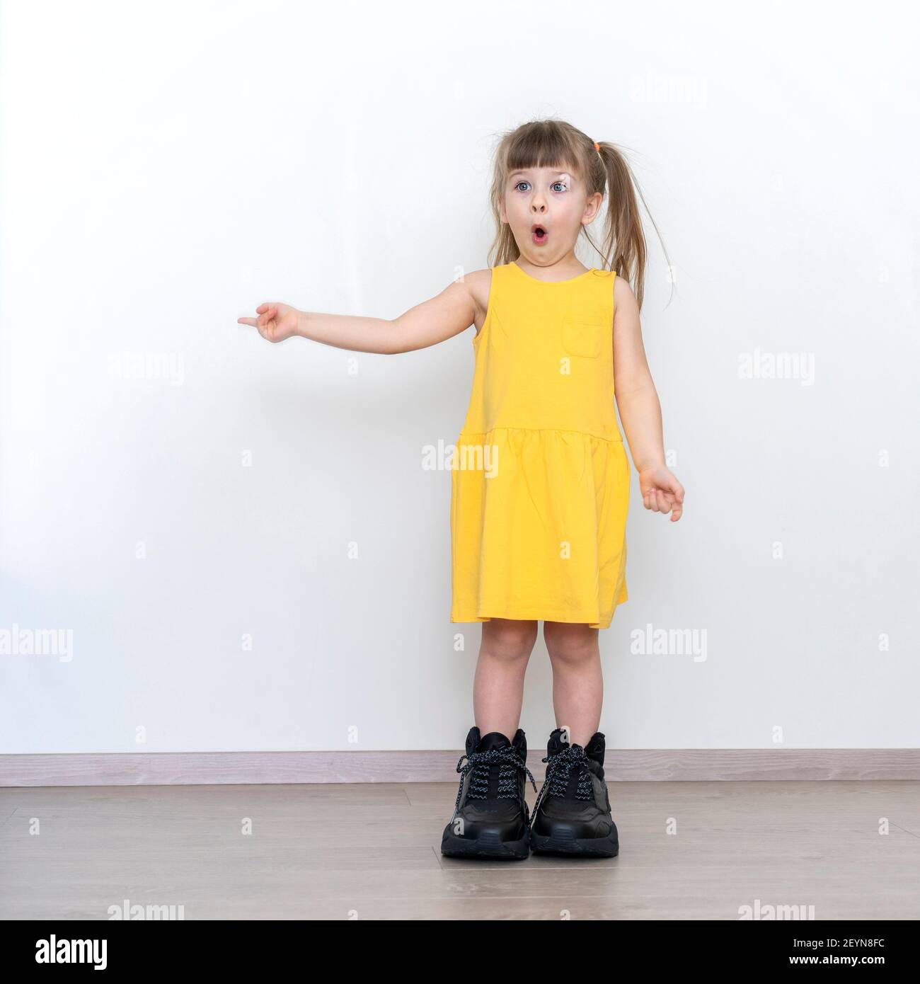 emocional niña con vestido amarillo y botas de hombre grandes señala a un  espacio vacío cerca de él, un lugar para su texto Fotografía de stock -  Alamy