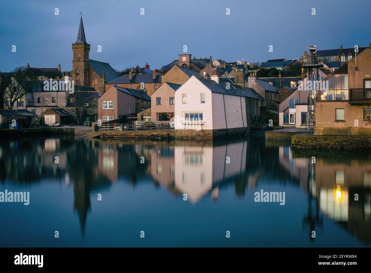 Vista desde el lado del agua de las casas escocesas en las islas Orkney con los edificios reflejos en el agua por la mañana Foto de stock