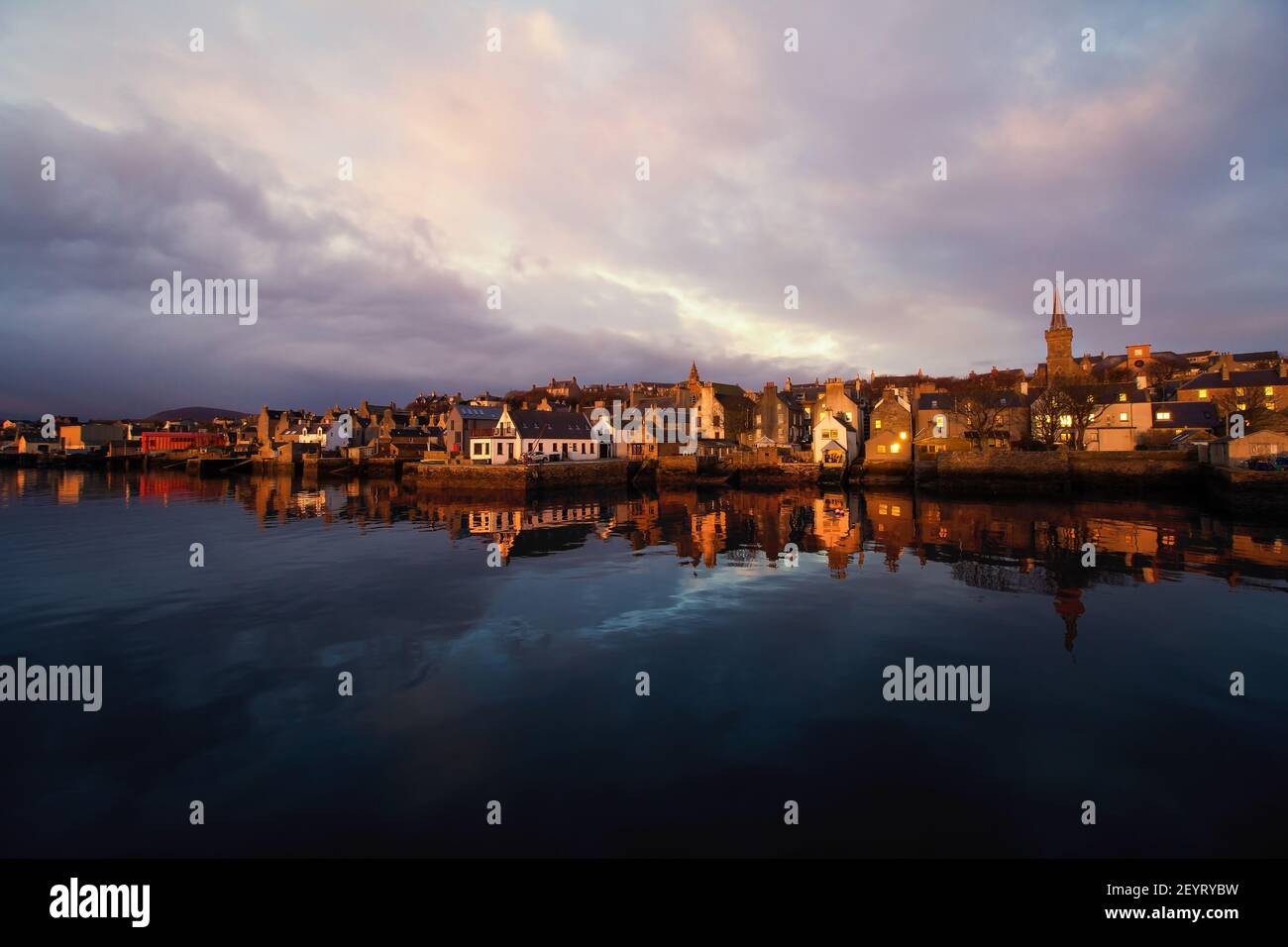 La luz de la mañana dorada golpea las casas antiguas frente al mar en la isla de Orkney En el norte de Escocia con agua azul oscuro y cielo brillante Foto de stock