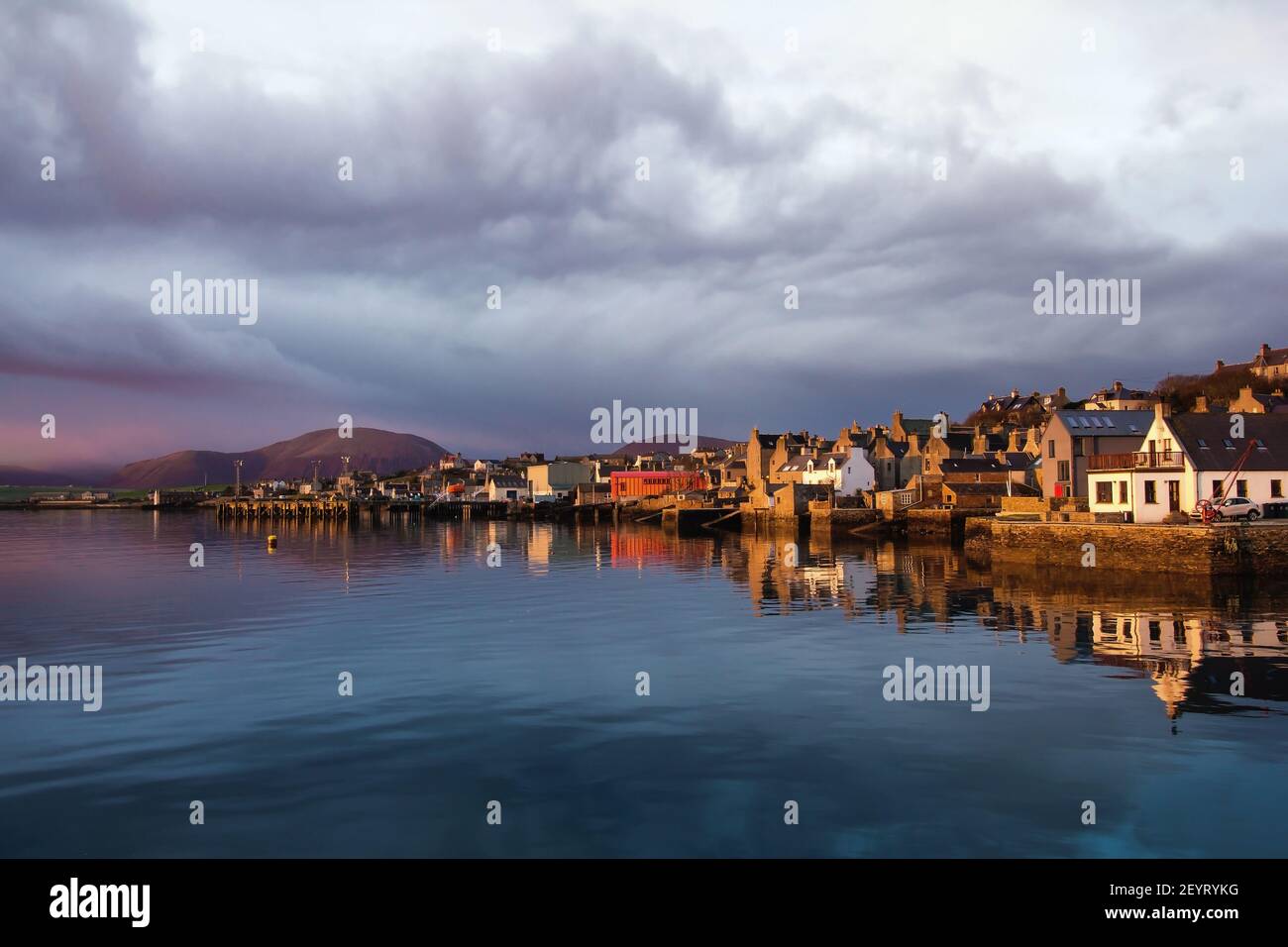 Luz de la mañana con casas antiguas frente al mar en la isla de Orkney norte de Escocia con agua azul y el cielo brillante por encima de la distancia colina Foto de stock