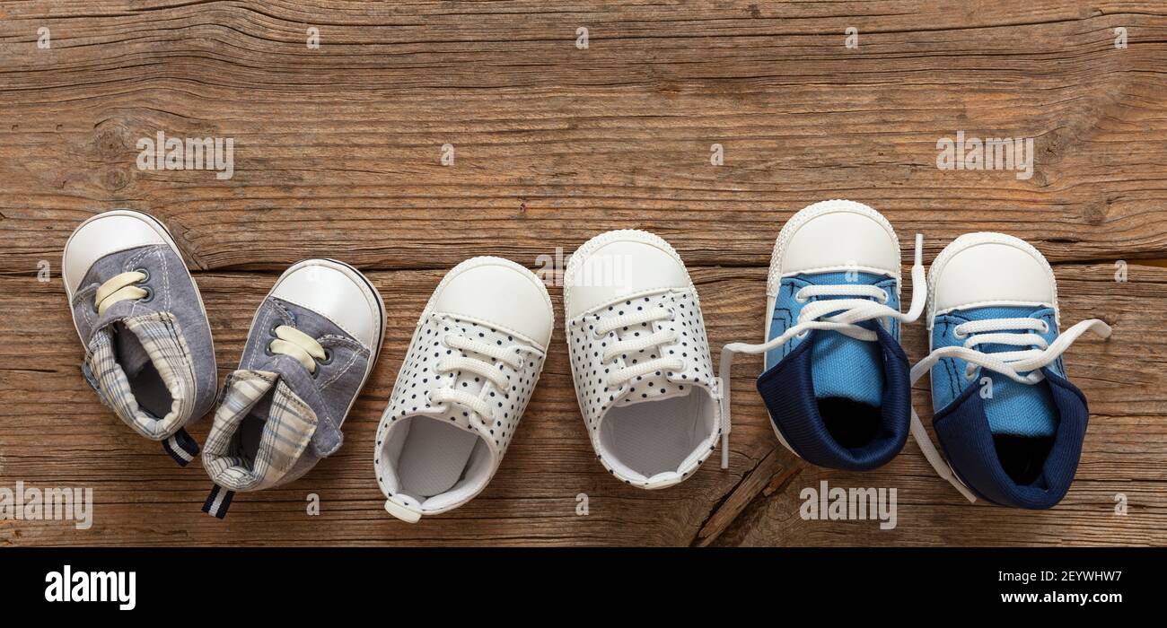 Primeros pasos del bebé. Tres pares de zapatos de niño variedad en el fondo  de madera del piso, vista superior. Calzado para niños, botas de bebé y zapatos  blandos para bebés seguidos