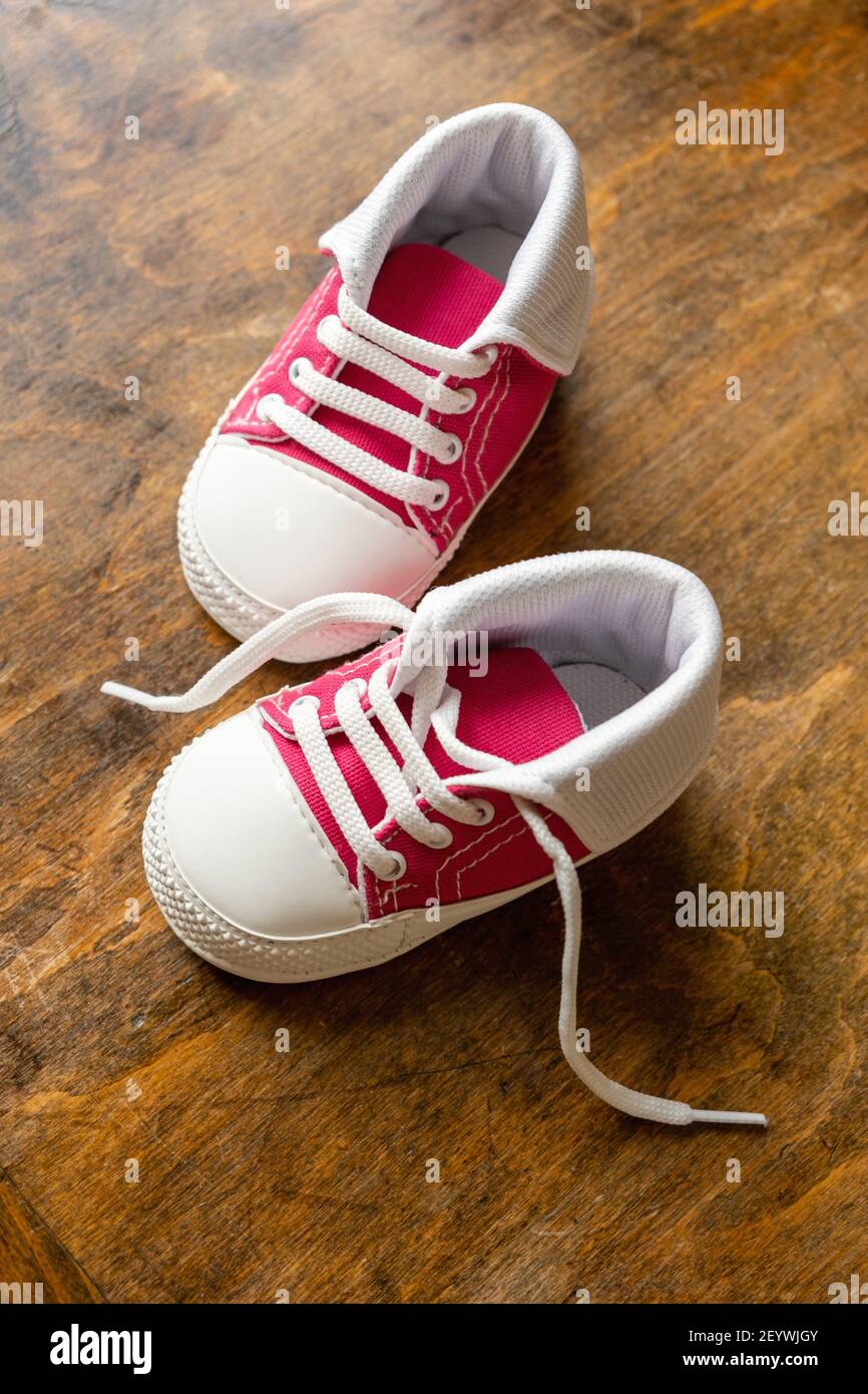 Zapatos deportivos para bebés sobre suelo de madera. Niño pequeño tamaño  rosa rojo sneakers, botitas de lona vista de primer plano. Vertical  Fotografía de stock - Alamy