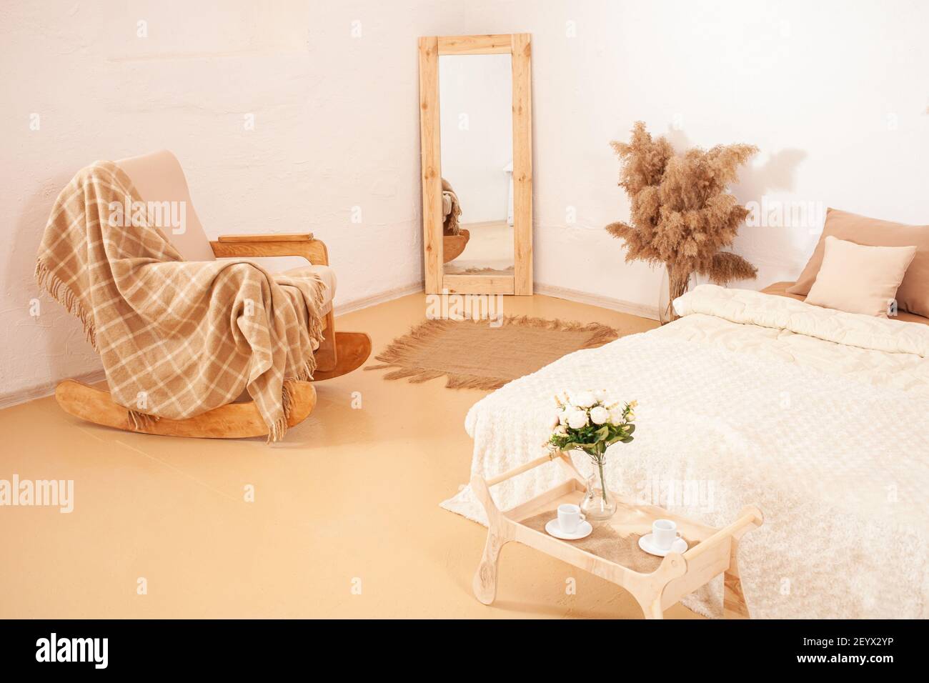 Interior blanco marrón beige. Dormitorio de tonos claros. Una mecedora con  un plaid, un espejo en un marco de madera, flores pampas planta.  Decoraciones para t Fotografía de stock - Alamy