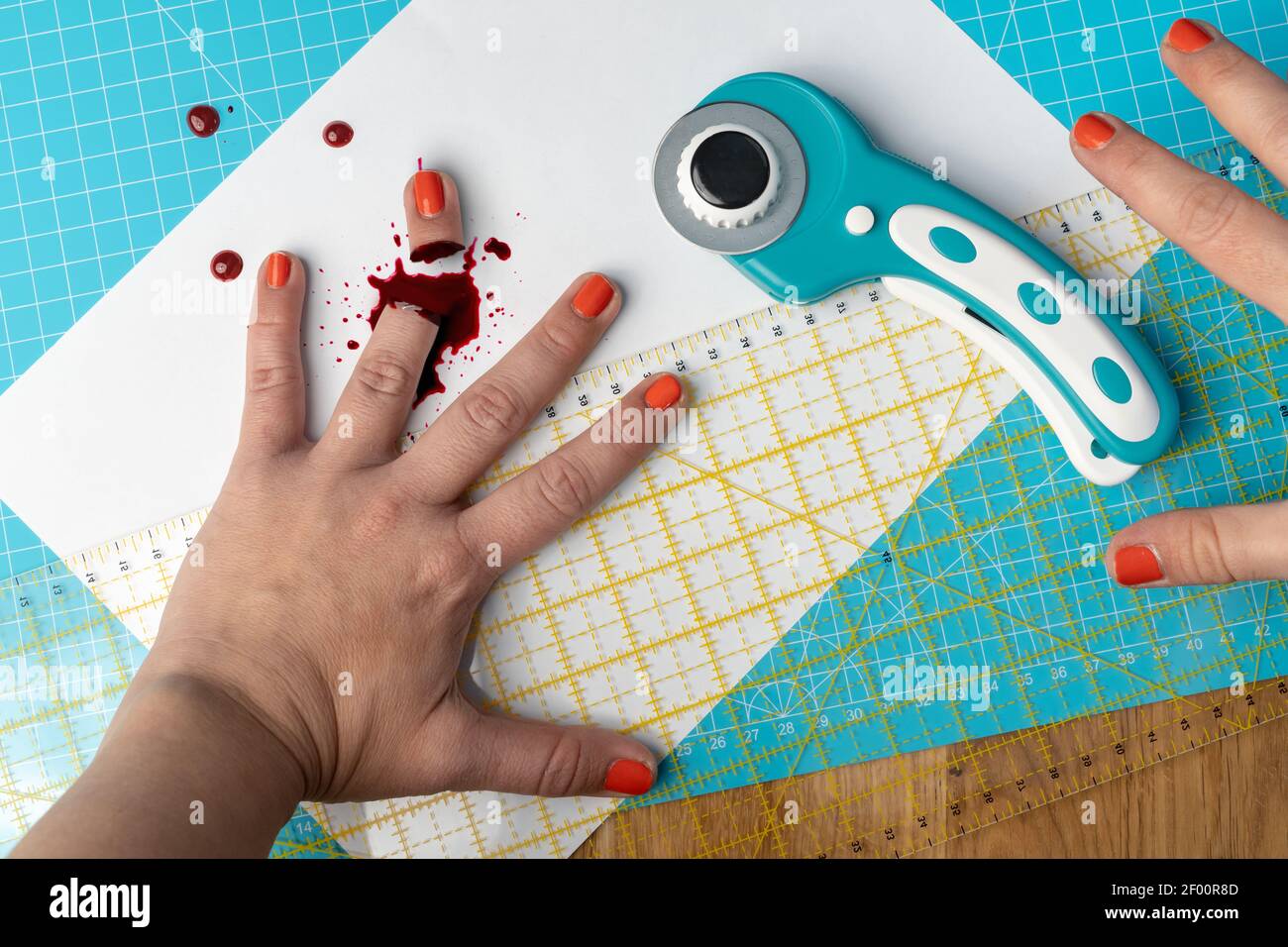 Una mujer con esmalte de uñas de color naranja picó su dedo una cortadora giratoria mientras se utiliza una estera de corte azul brillante y una regla Foto de stock