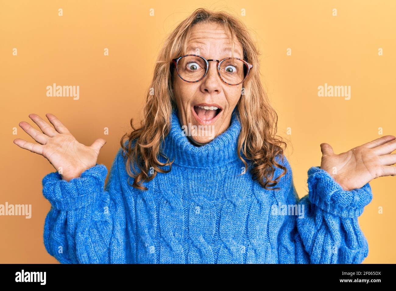 Mujer rubia de mediana edad con gafas y suéter de invierno informal  celebrando loco y asombrado por el éxito con los brazos levantados y. ojos  abiertos gritando ex Fotografía de stock -