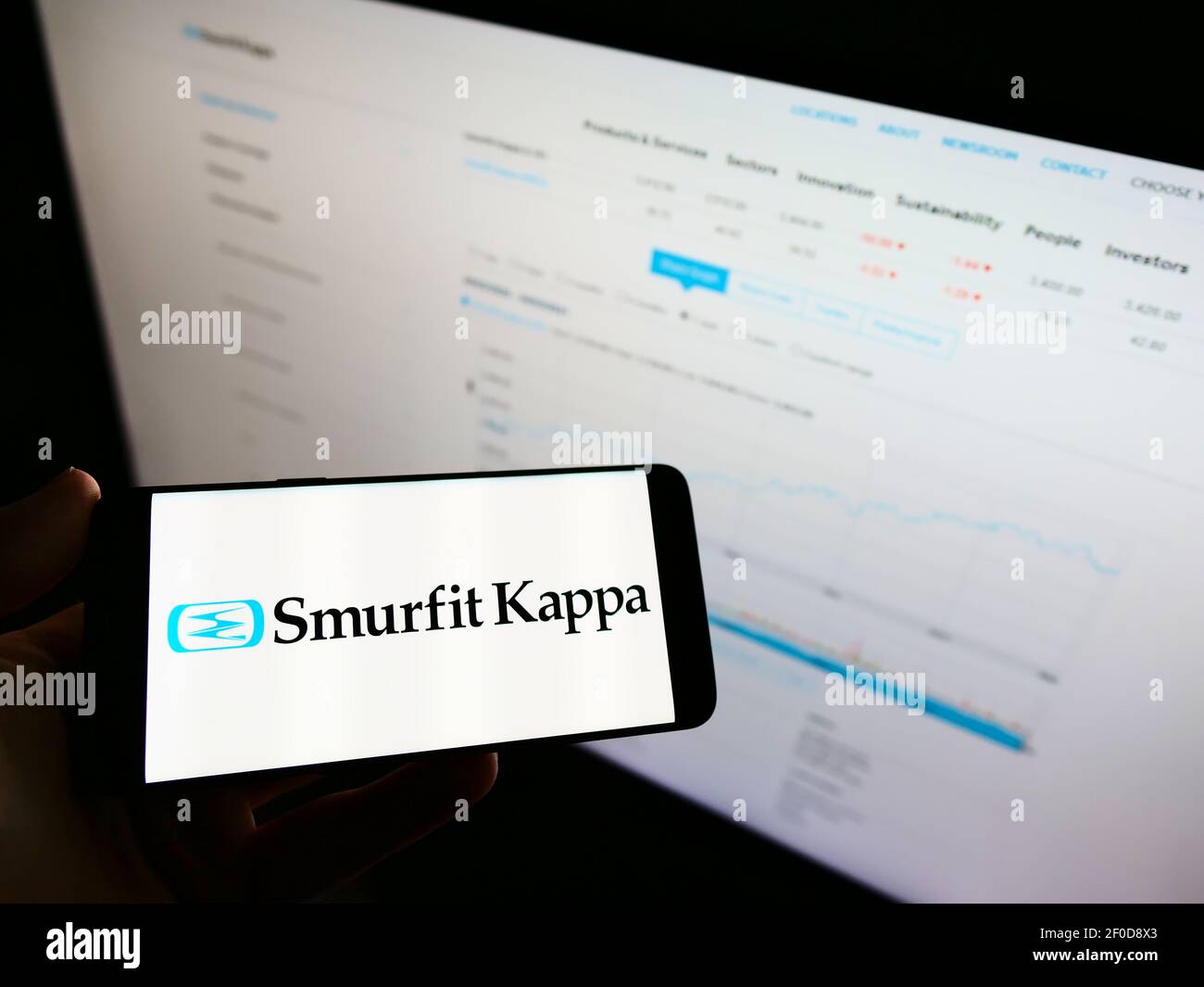 Persona que sostiene el teléfono celular con el logotipo de la empresa  irlandesa de embalaje Smurfit Kappa Group en la pantalla delante de la  página web con la carta. Enfoque en la