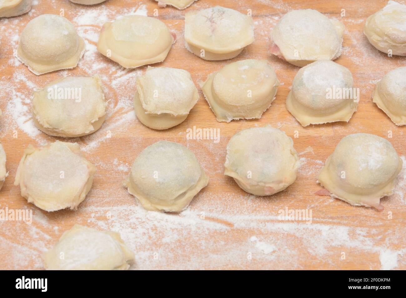 Dumplings caseros con carne sobre mesa de madera con harina. Ravioli para cocinar la cena. Primer plano, enfoque selectivo. Foto de stock