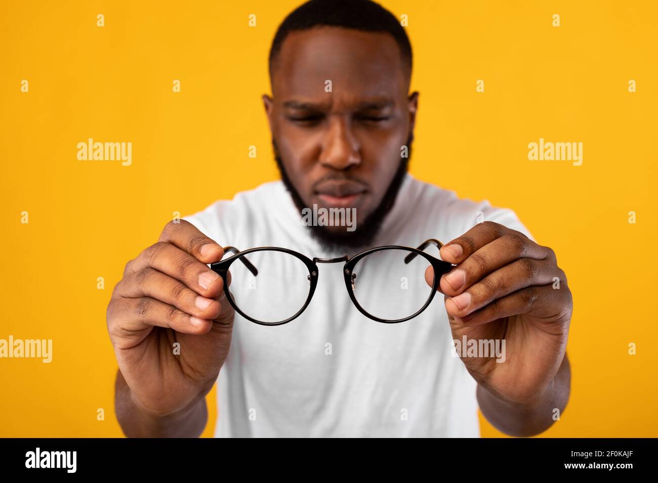 Hombre sosteniendo gafas escillando ojos con mala vista, fondo amarillo Foto de stock