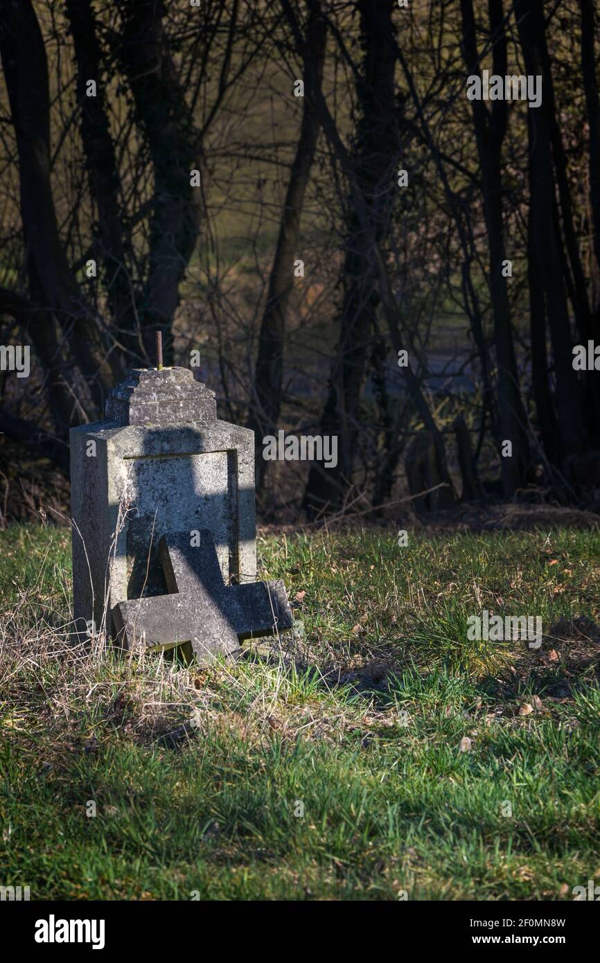 Antigua lápida con cruz rota pero con una sombra en forma de cruz bajo los árboles en un cementerio abandonado, símbolo religioso, espacio de copia, foco seleccionado Foto de stock