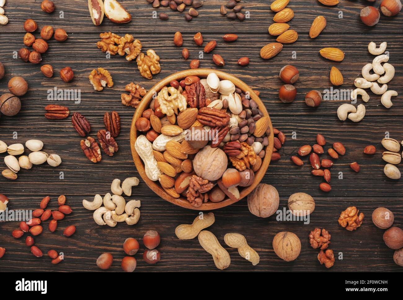 Surtido de frutos secos en cuencos. Anacardos, avellanas, nueces, pistachos, pacanas, nueces de pino, cacahuetes, macadamia, almendras, nueces de brasil. Mezcla de alimentos en madera Foto de stock