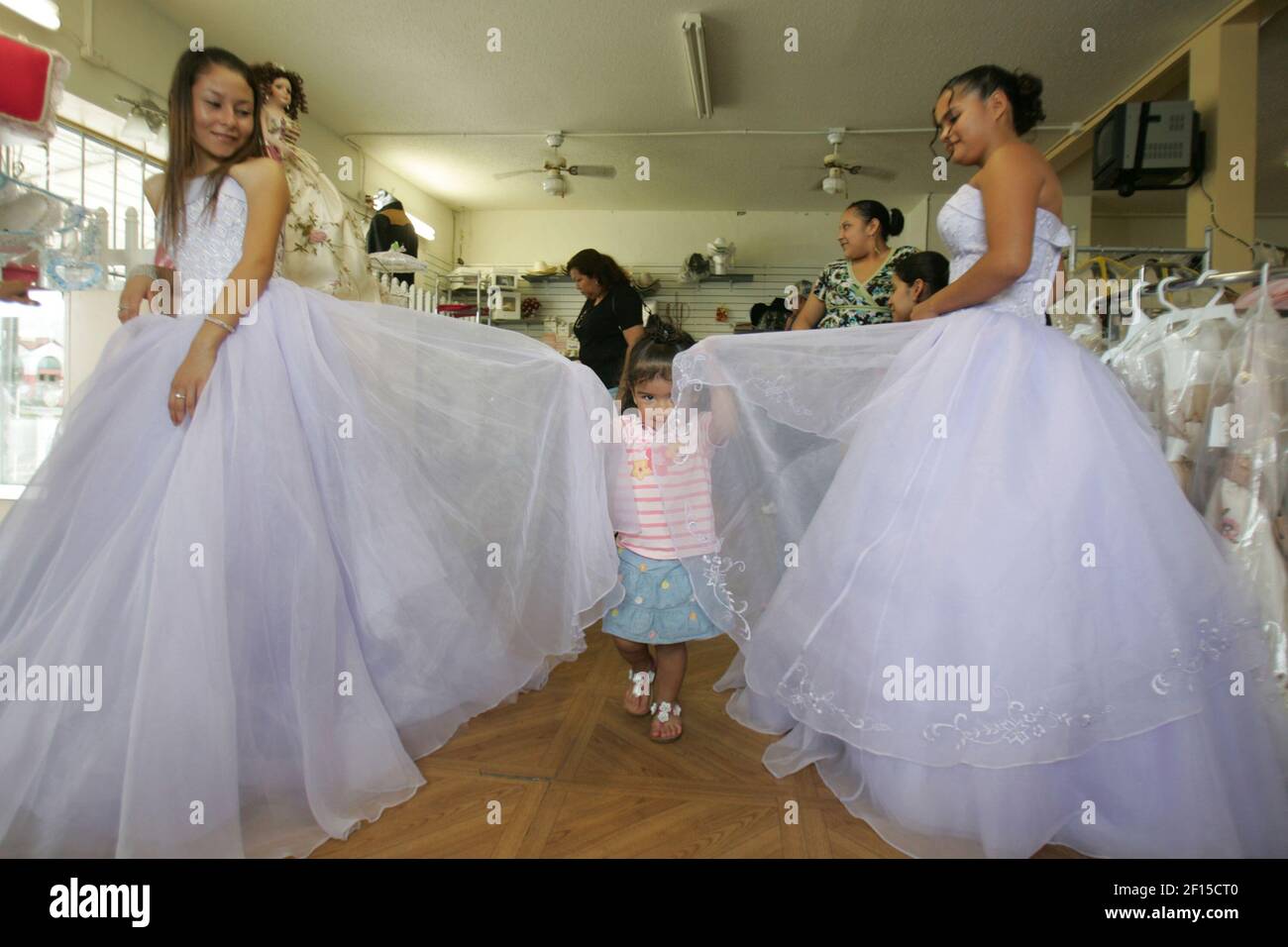 Yaritza Estrada, 2, centro, agarra los vestidos de Wendy Acosta, 15,  izquierda, y Sylvia Cárdenas, 16, En la tienda de membrillos en de Leon  Springs, Florida, 20 de junio de 2007. Acosta