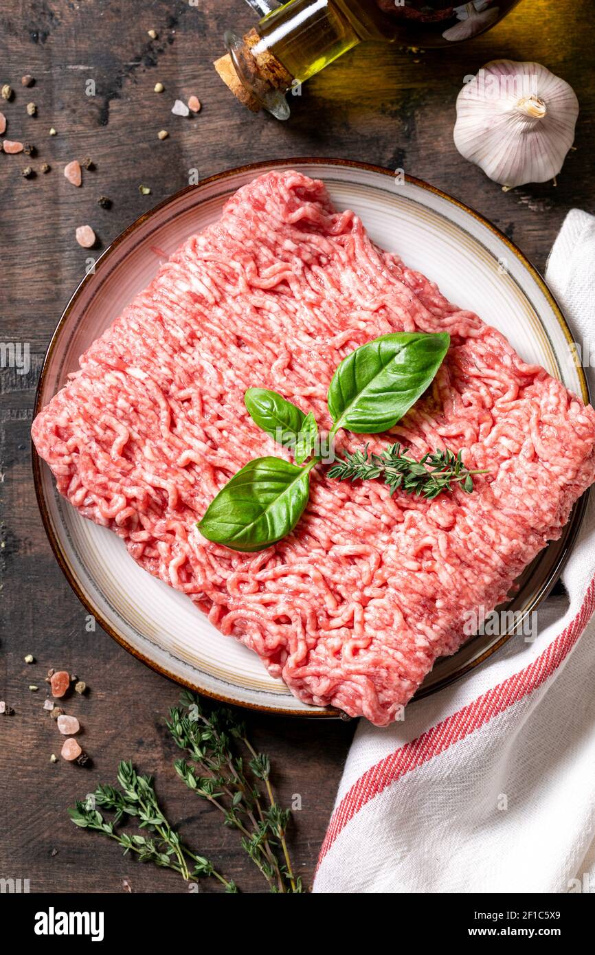 Carne picada fresca cruda sobre un plato y fondo de madera. Foto de stock