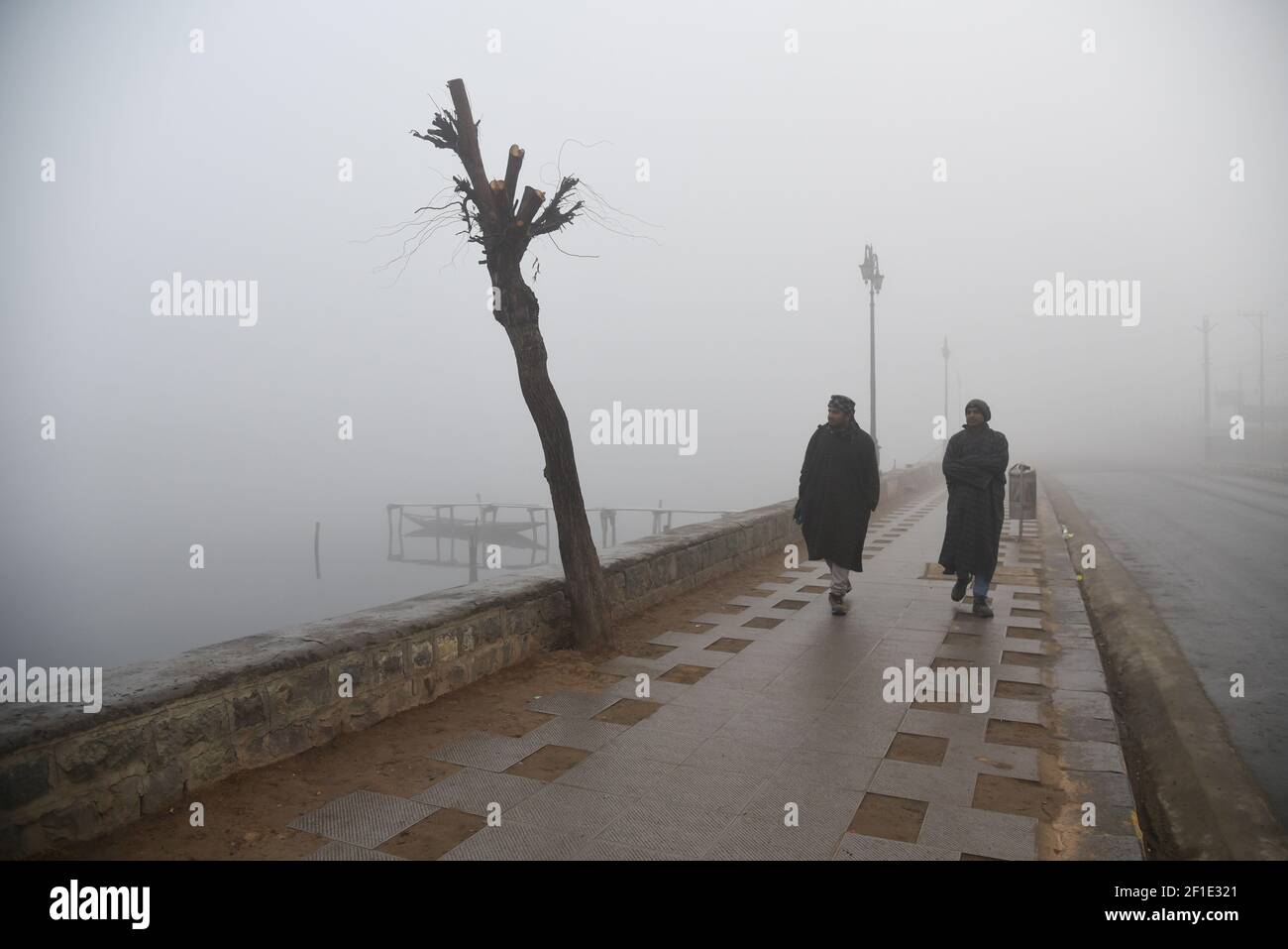 La gente camina a lo largo de la orilla del lago Dal durante una mañana foggy en Srinagar. Las temperaturas nocturnas a través de Cachemira cayeron por debajo del punto de congelación. Mañana frío y niebla densa mantuvo la mayoría de los cachemiros en el interior hasta que un sol débil comenzó a luchar su camino a través de una capa delgada de nubes de invierno. (Foto de Irnes Abbas / SOPA Images/Sipa USA) Foto de stock