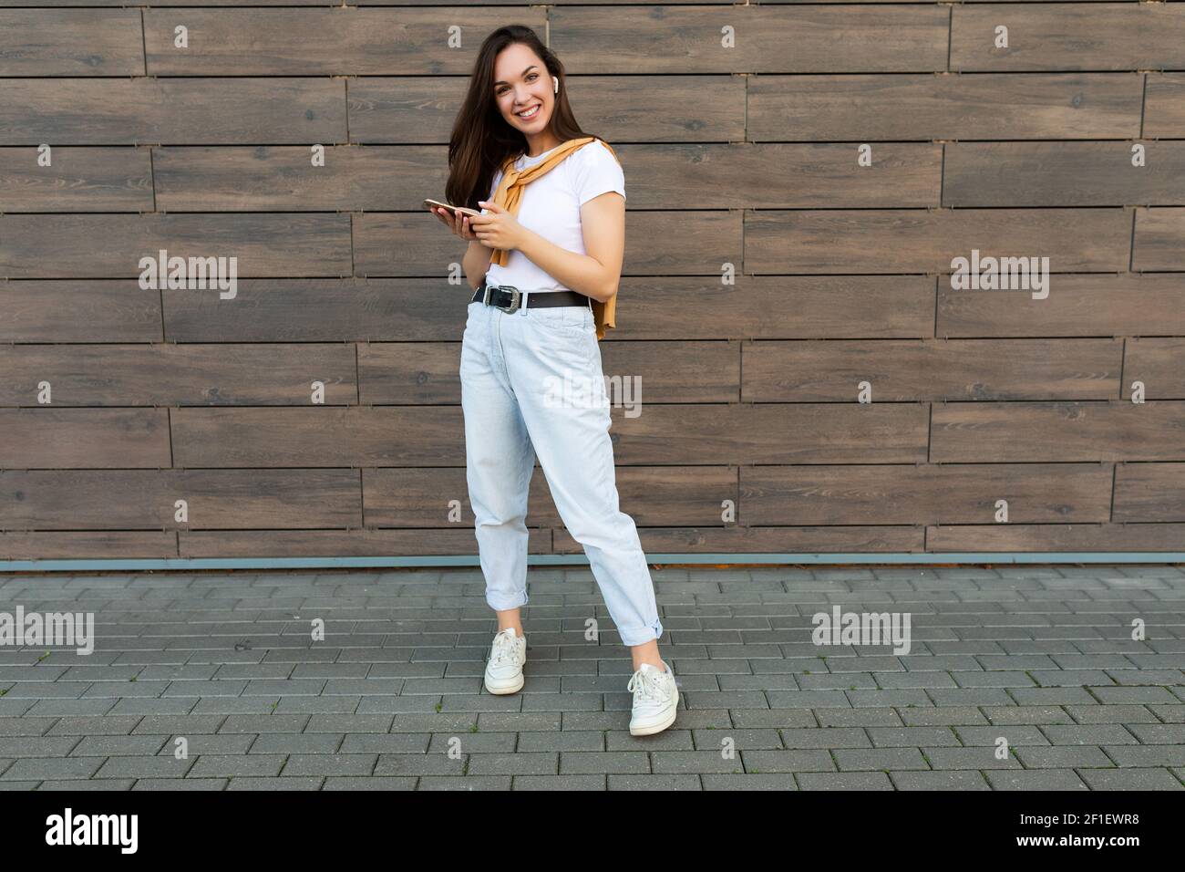 Foto de cuerpo entero de una bonita mujer morena adultappy llevar ropa  informal y escuchar música a través de auriculares inalámbricos de pie en  el Fotografía de stock - Alamy