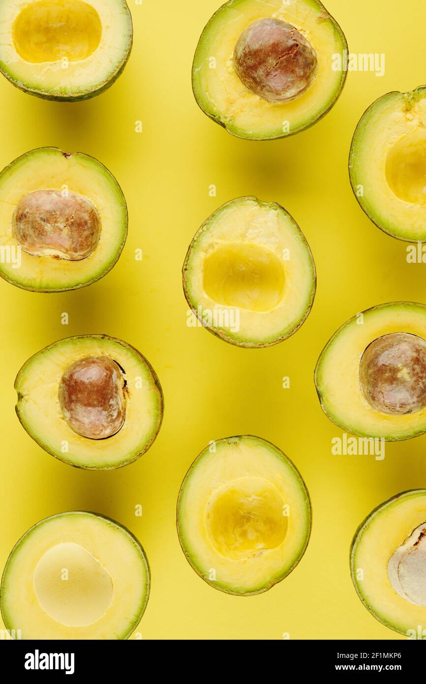 Aguacates maduros frescos cortados con y sin núcleos en amarillo superficie Foto de stock