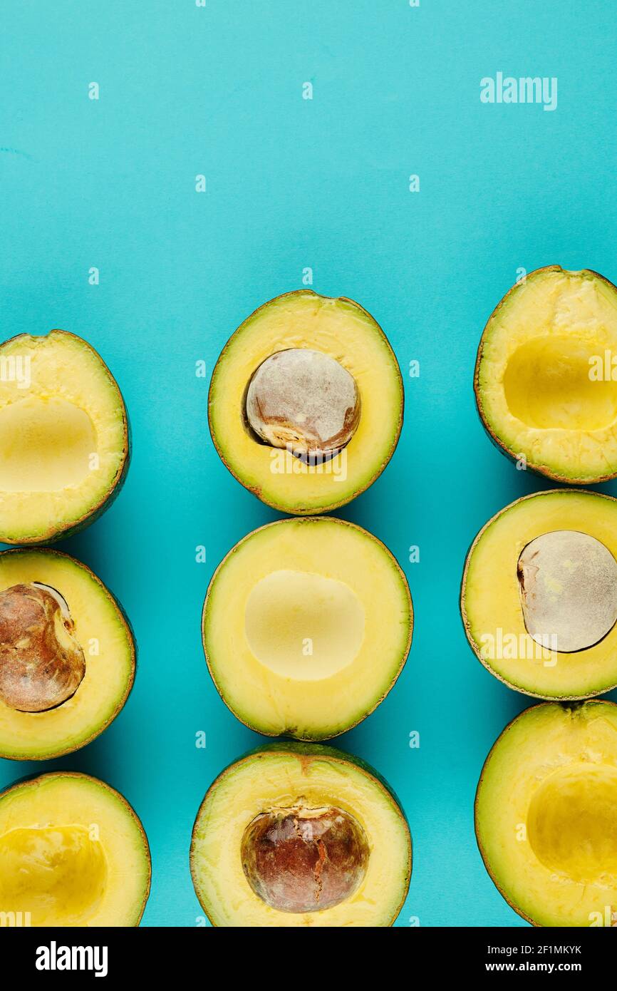 Aguacates maduros de corte delicado con y sin núcleos en luz fondo azul Foto de stock