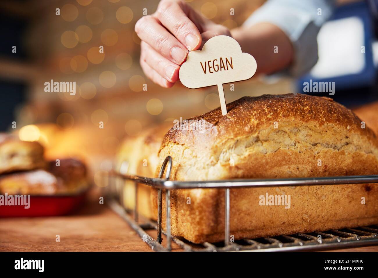 Asistente de ventas en panadería poniendo la etiqueta Vegan en recién horneado Panes de masa de calabaza horneados Foto de stock