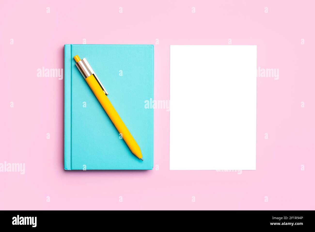 escritorio con bloc de notas azul, bolígrafo amarillo y papel blanco con copiar fondo de espacio sobre fondo rosa Foto de stock
