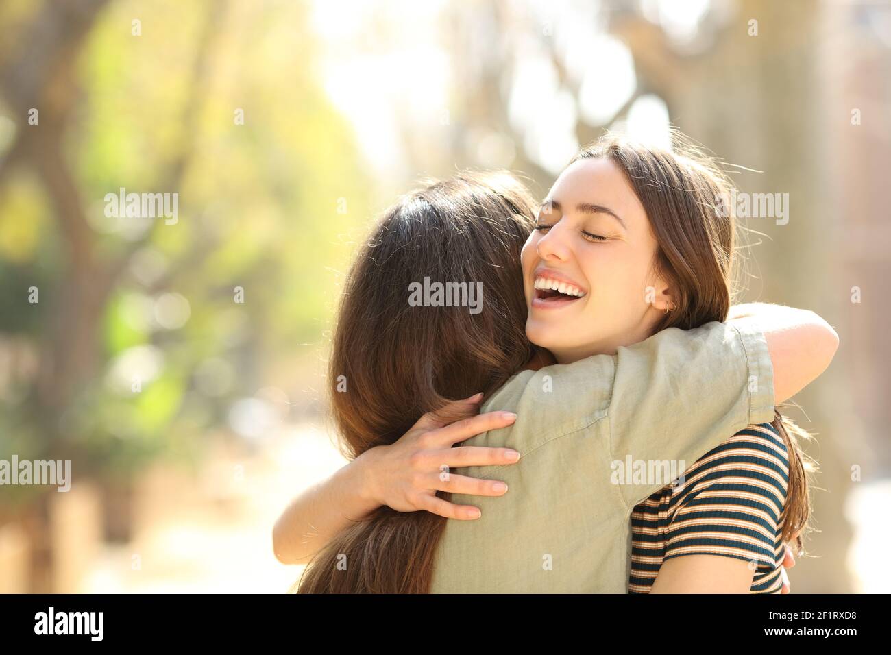 Dos mujeres felices abrazando después de encontrarse en la calle a día soleado Foto de stock